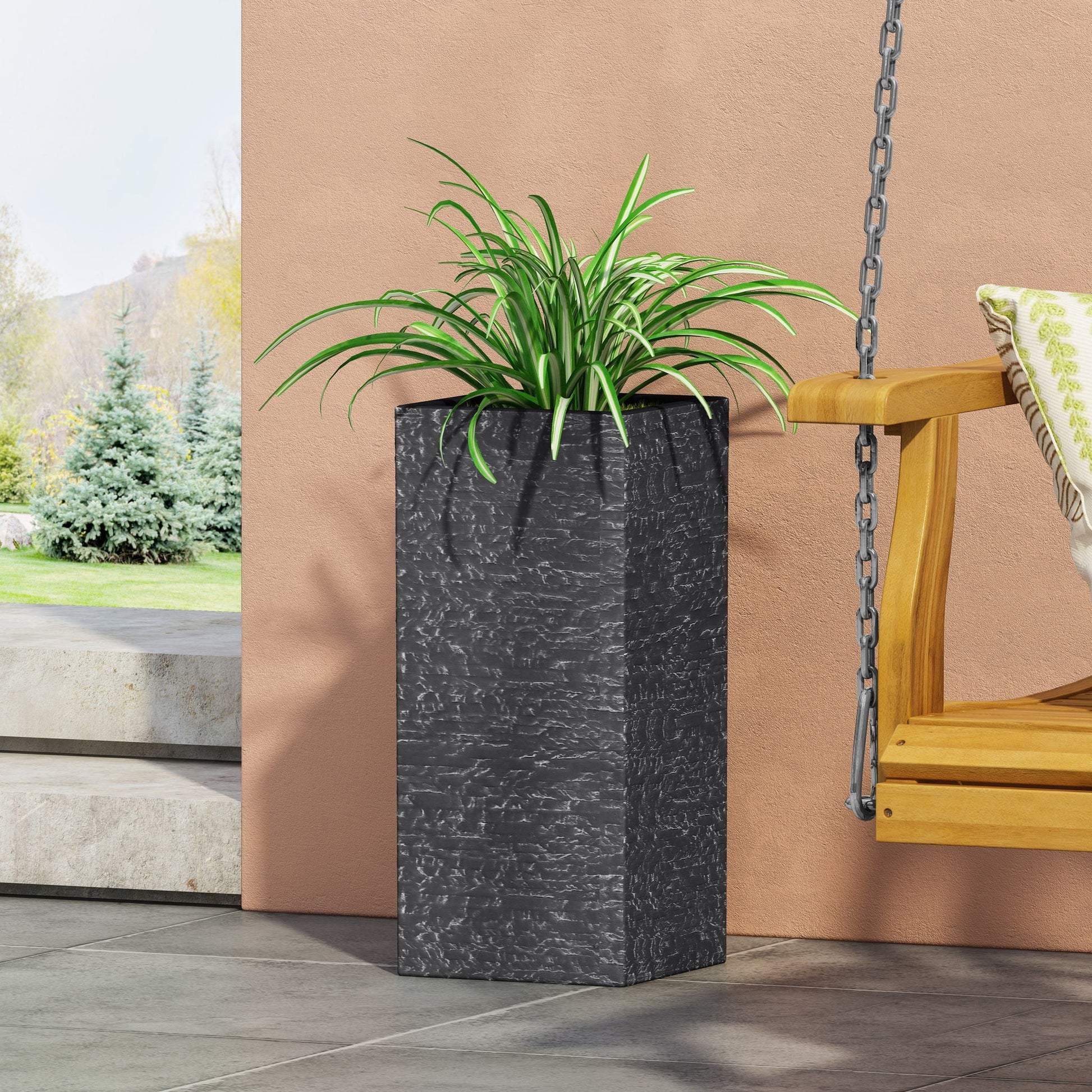Tall black planter with a green plant on a patio with a swing in the background.