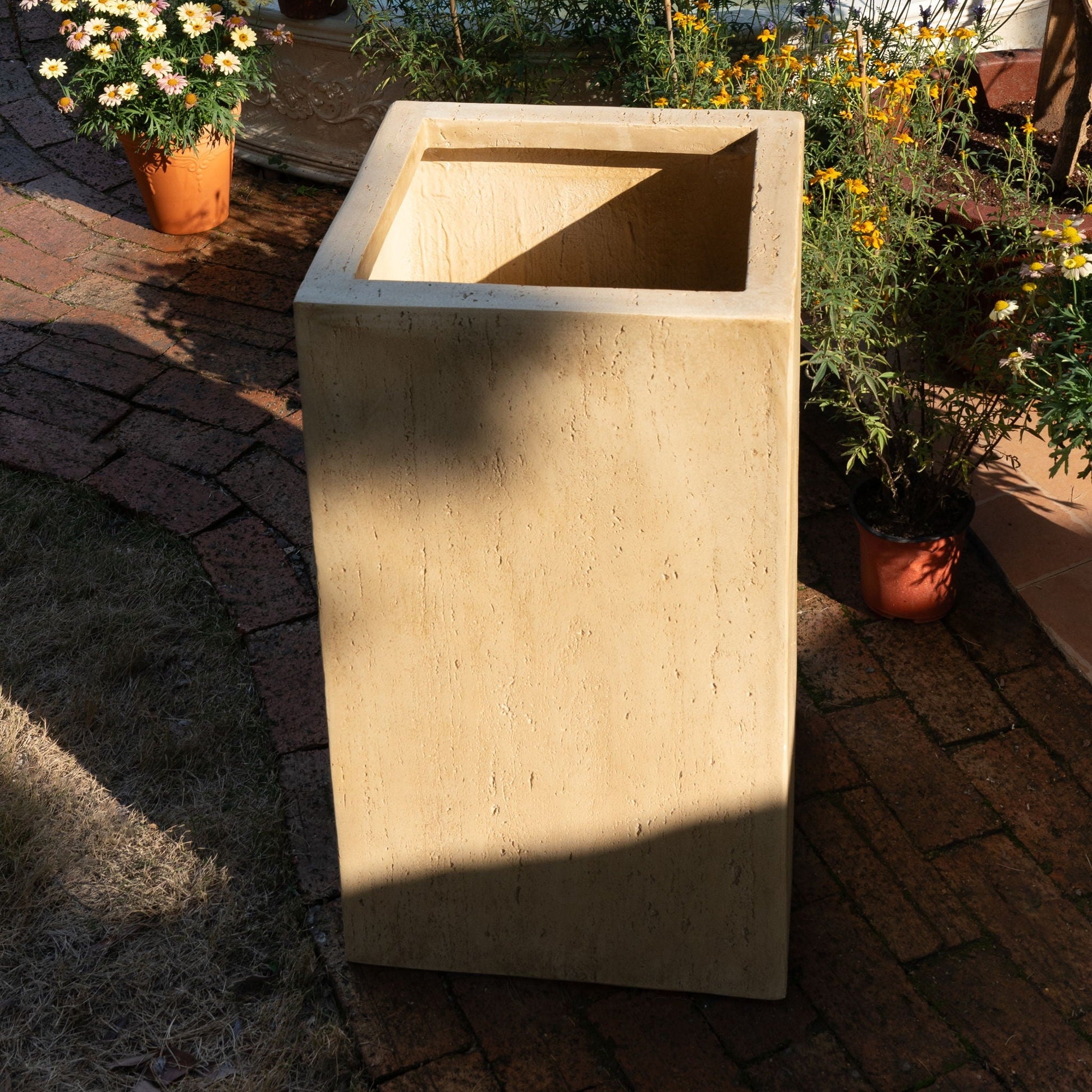 Beige rectangular planter box on a brick patio with potted plants around