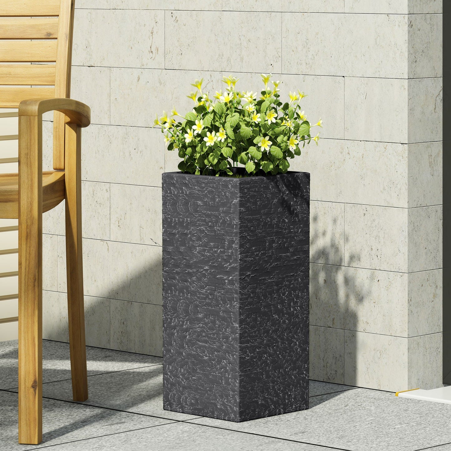 Tall dark gray planter with green plants against a light stone wall.