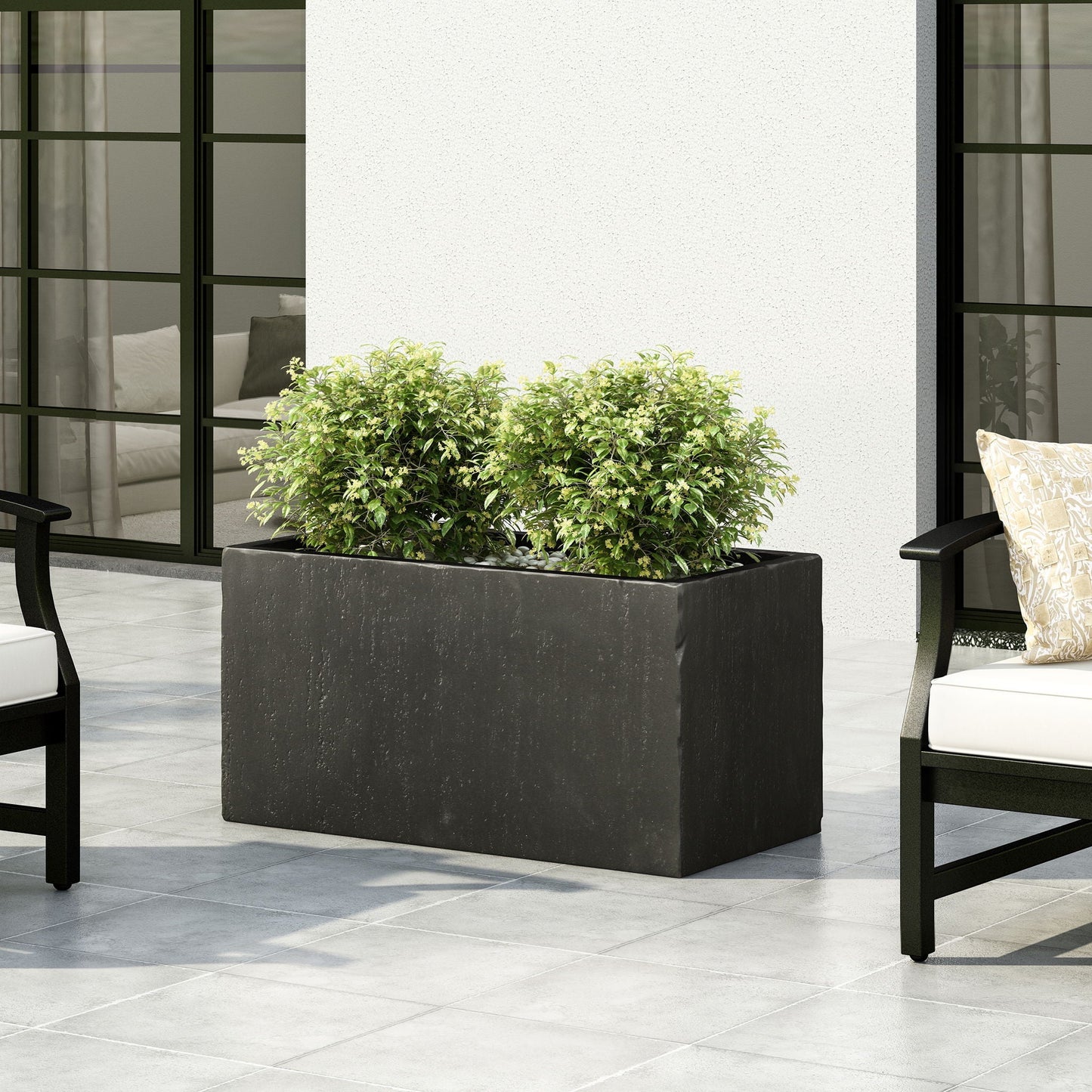Black rectangular planter with green plants on a patio with chairs and cushions.