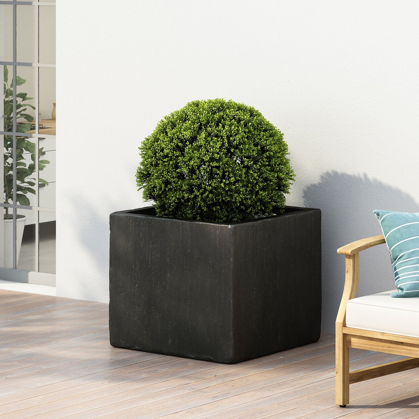 Square black planter with a green bush on a wooden deck next to a chair with a blue cushion.