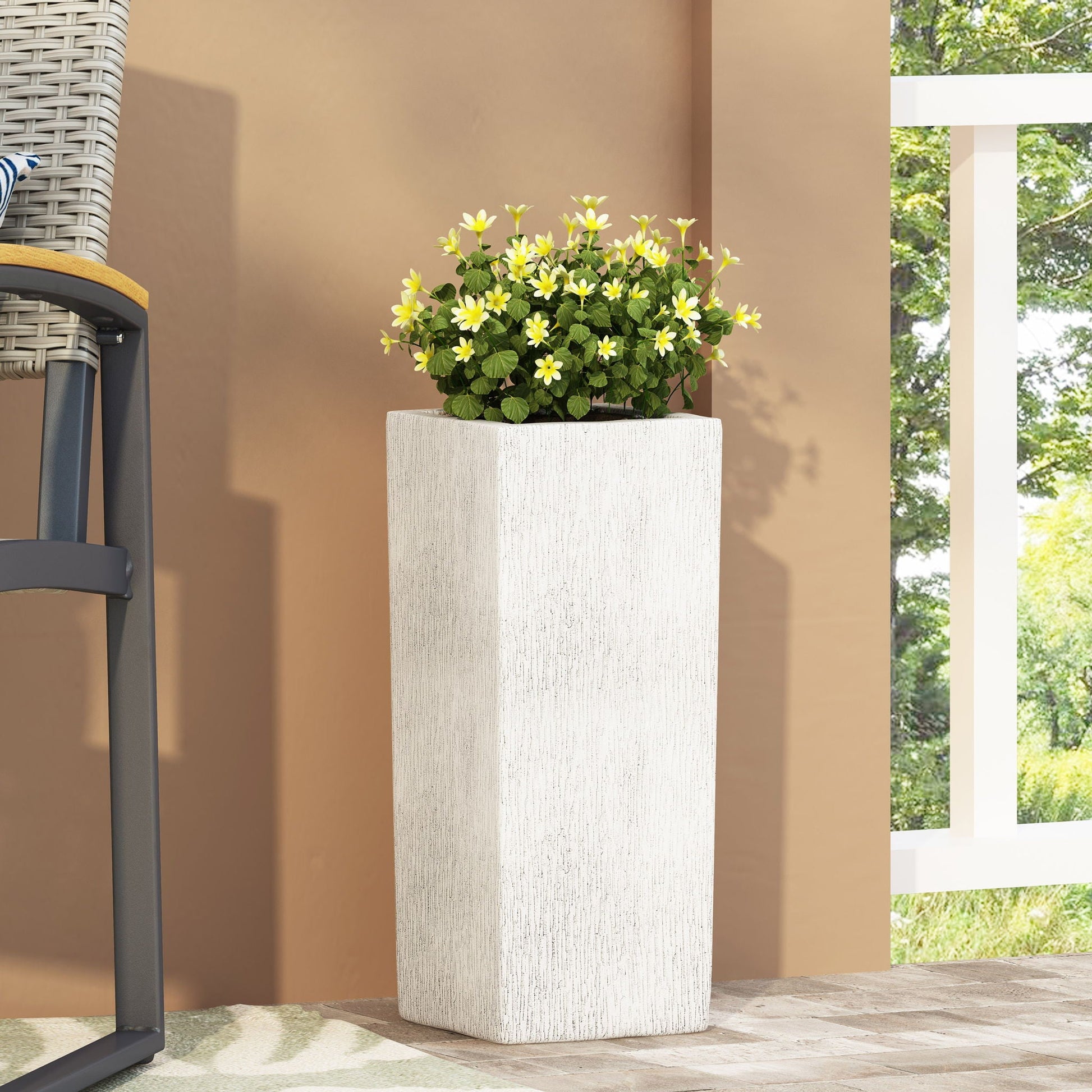 Tall white planter with green plant and yellow flowers on a patio