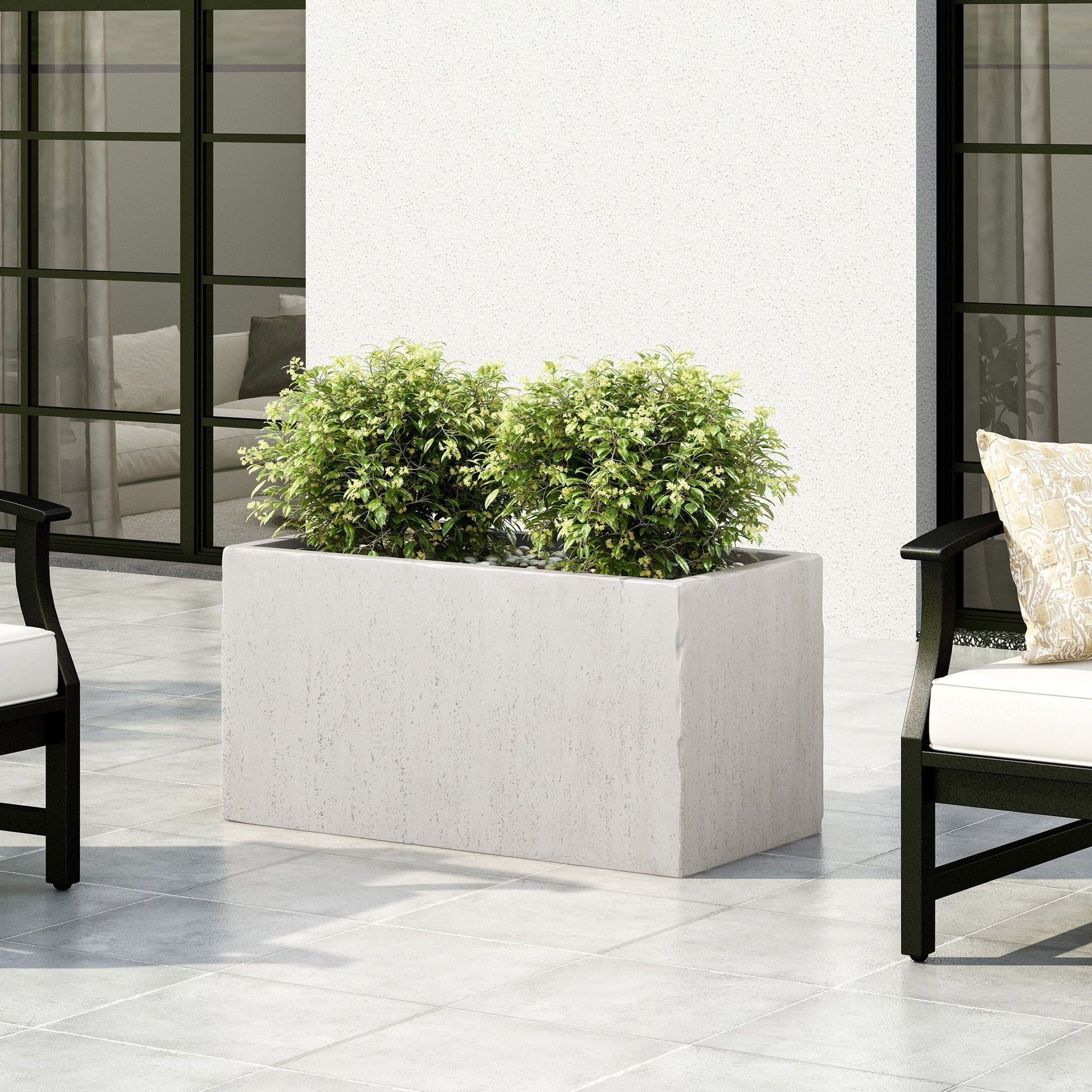 White rectangular planter with green plants on a patio with chairs and a couch.