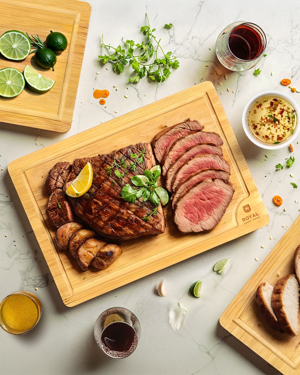 Sliced steak on a wooden cutting board with garnishes and drinks on a light surface