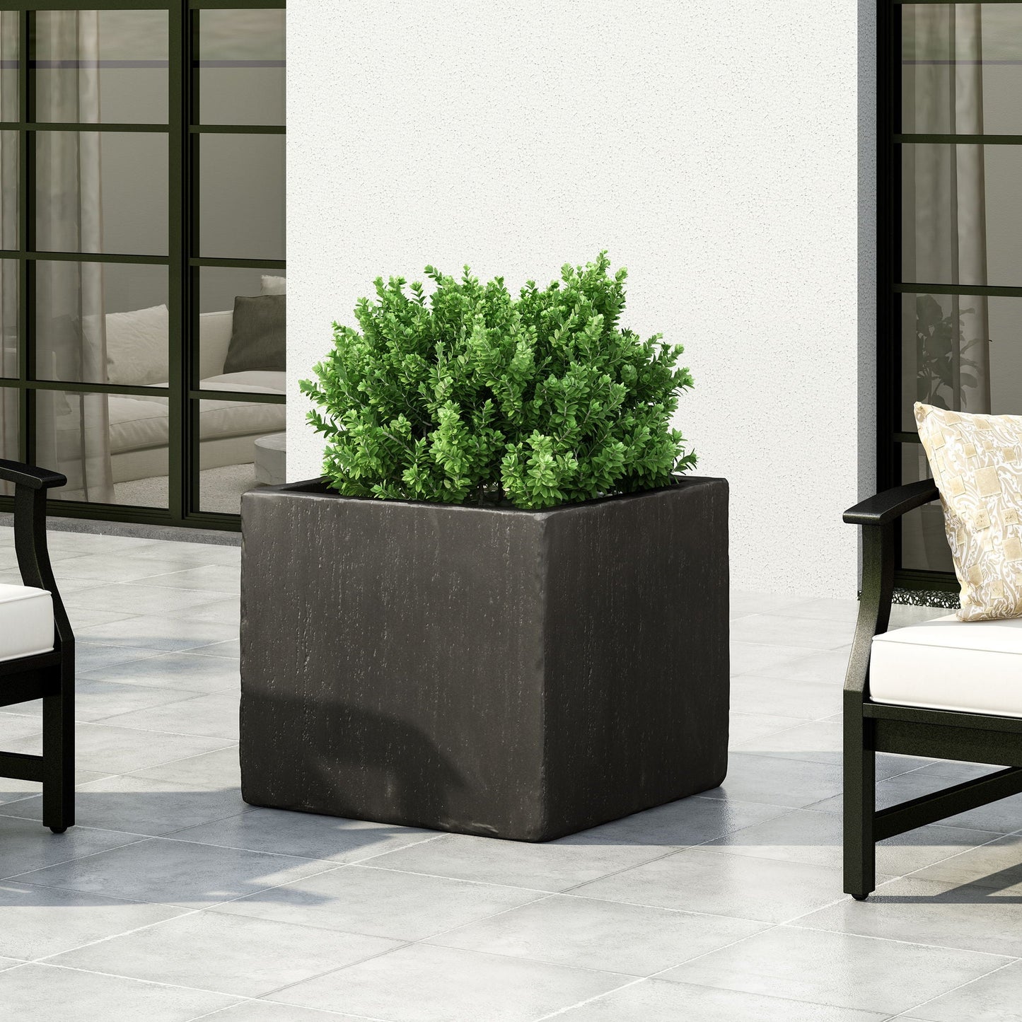 Square black planter with green plant on a patio with chairs and cushions.