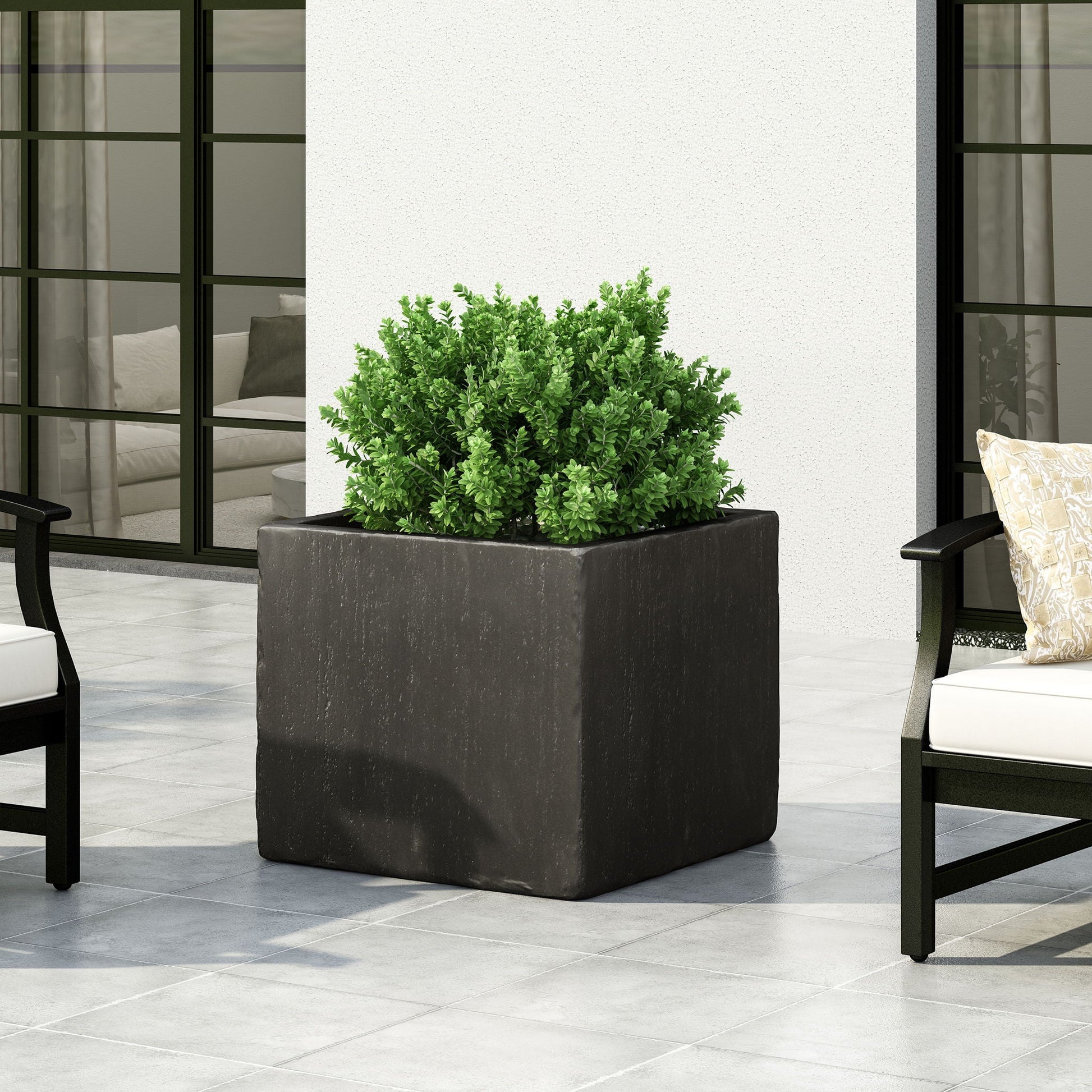 Square black planter with green plant on a patio with chairs and cushions.