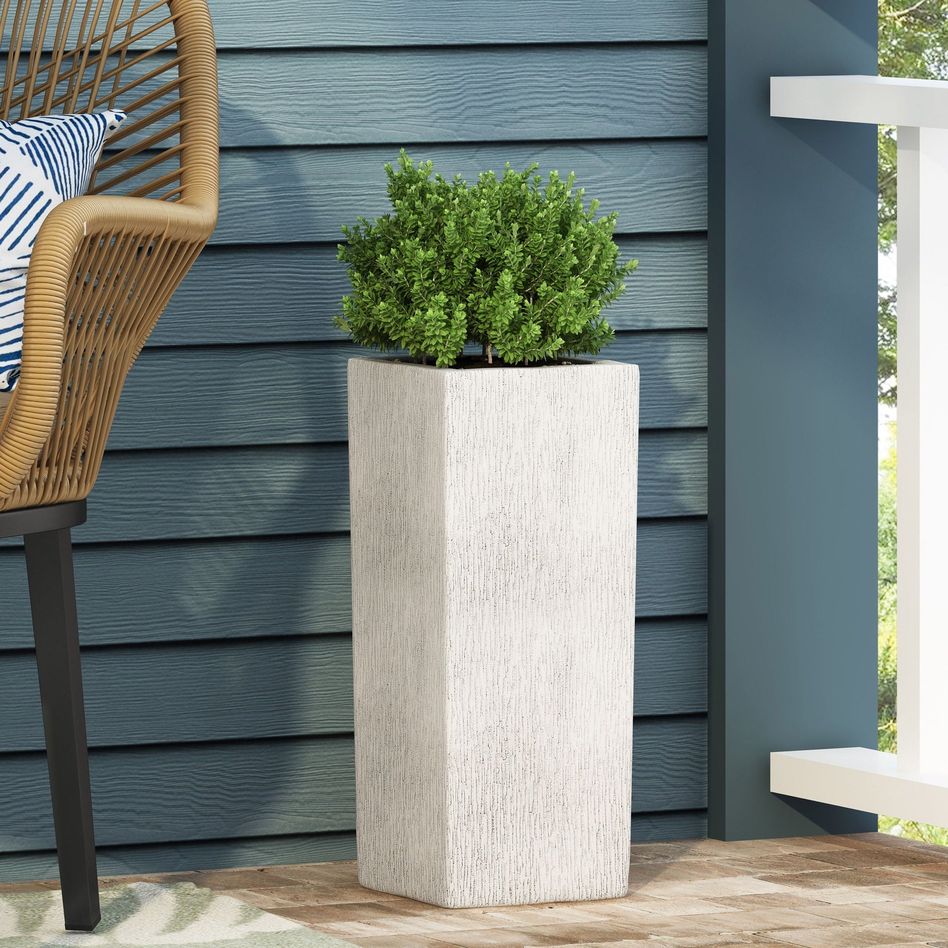 Tall rectangular planter with a green plant against a blue wall on a patio.