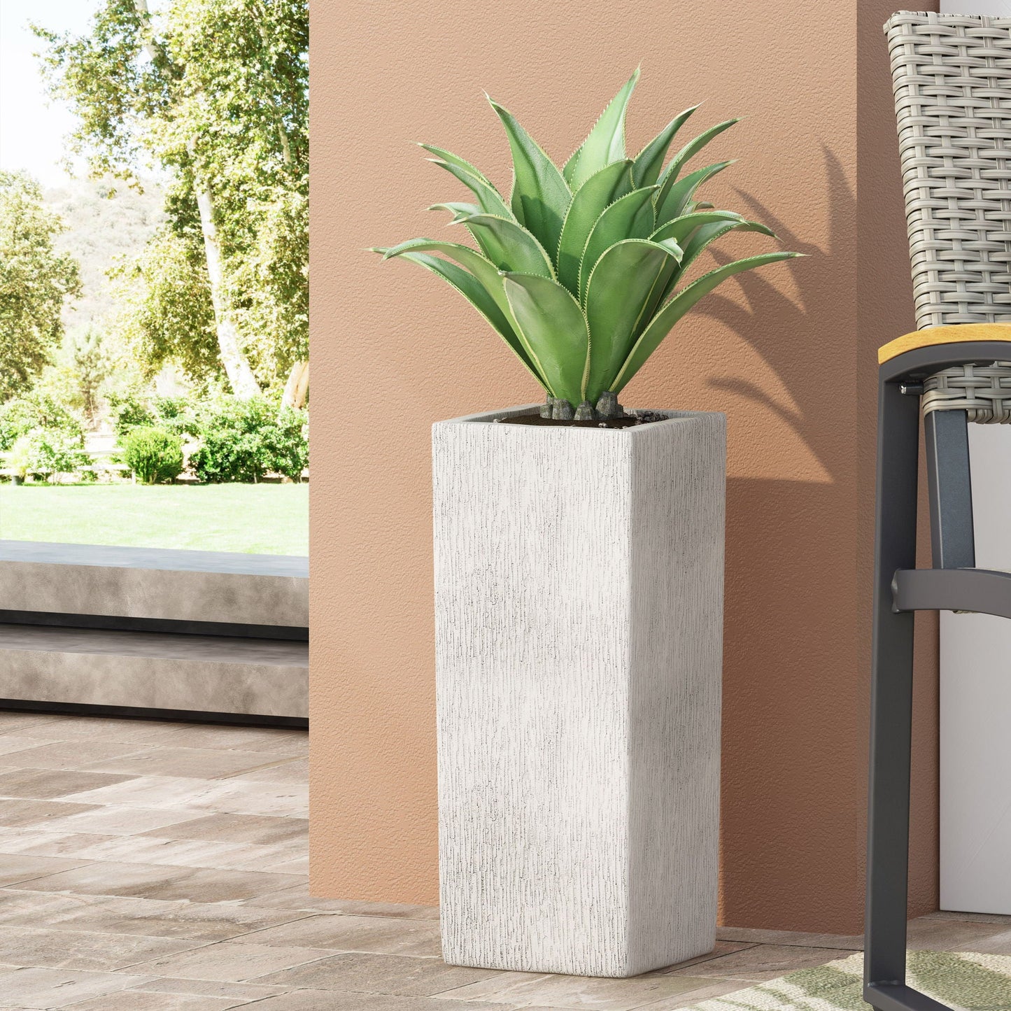 Potted plant in a textured white planter on a patio with a garden view.