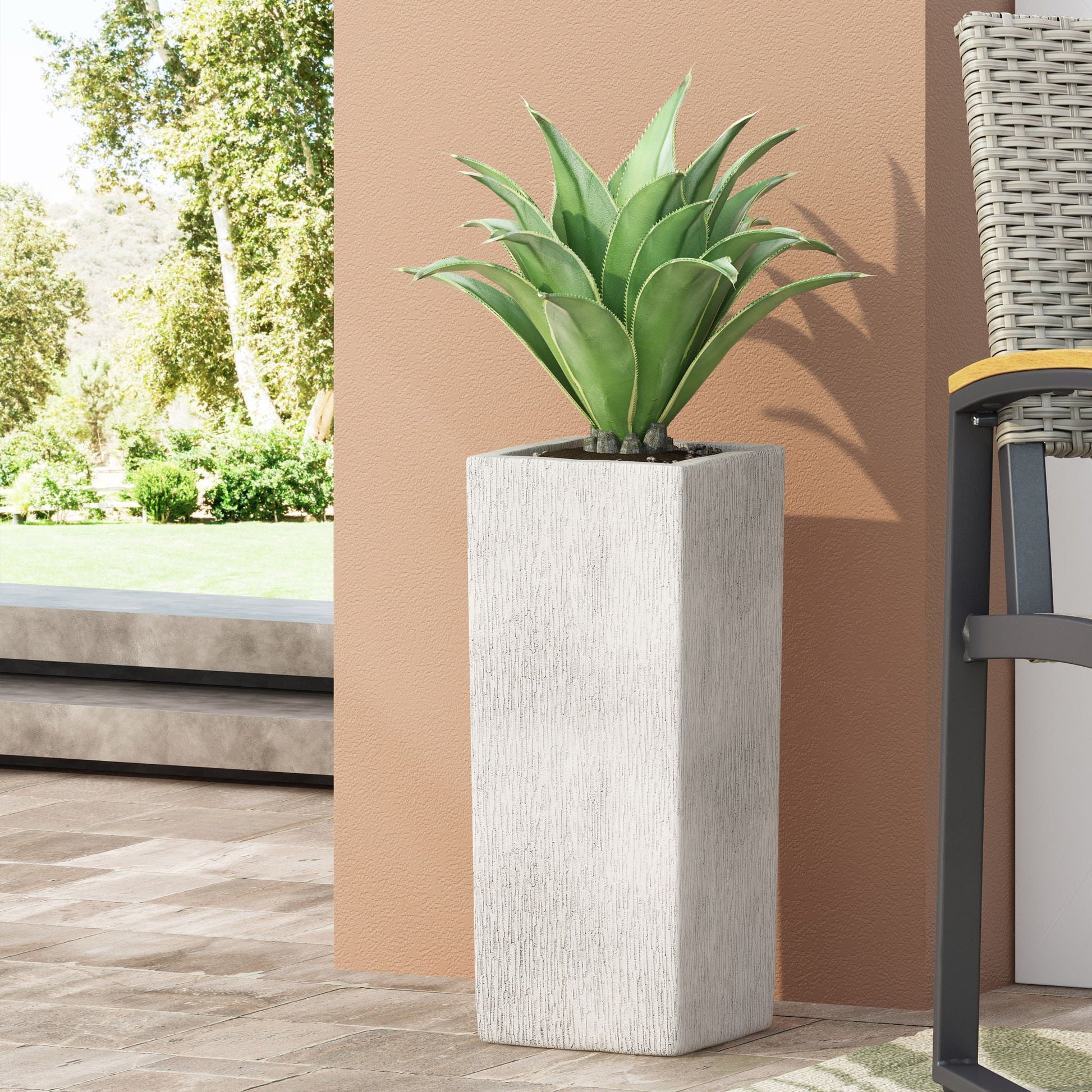 Potted plant in a textured white planter on a patio with a garden view.