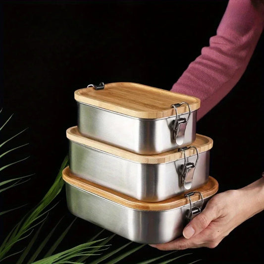 Stack of stainless steel food containers with wooden lids held by a person against a dark background.