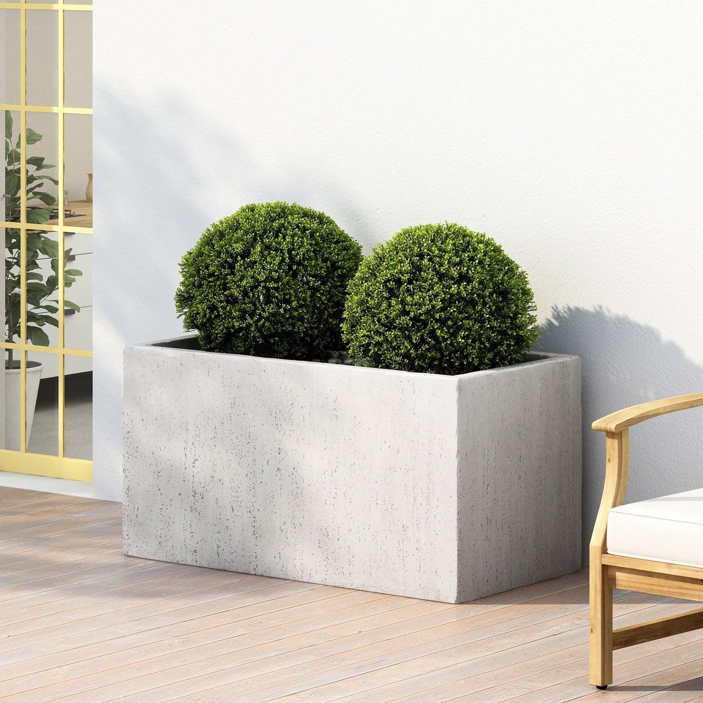 Two spherical green plants in a rectangular concrete planter on a wooden deck.
