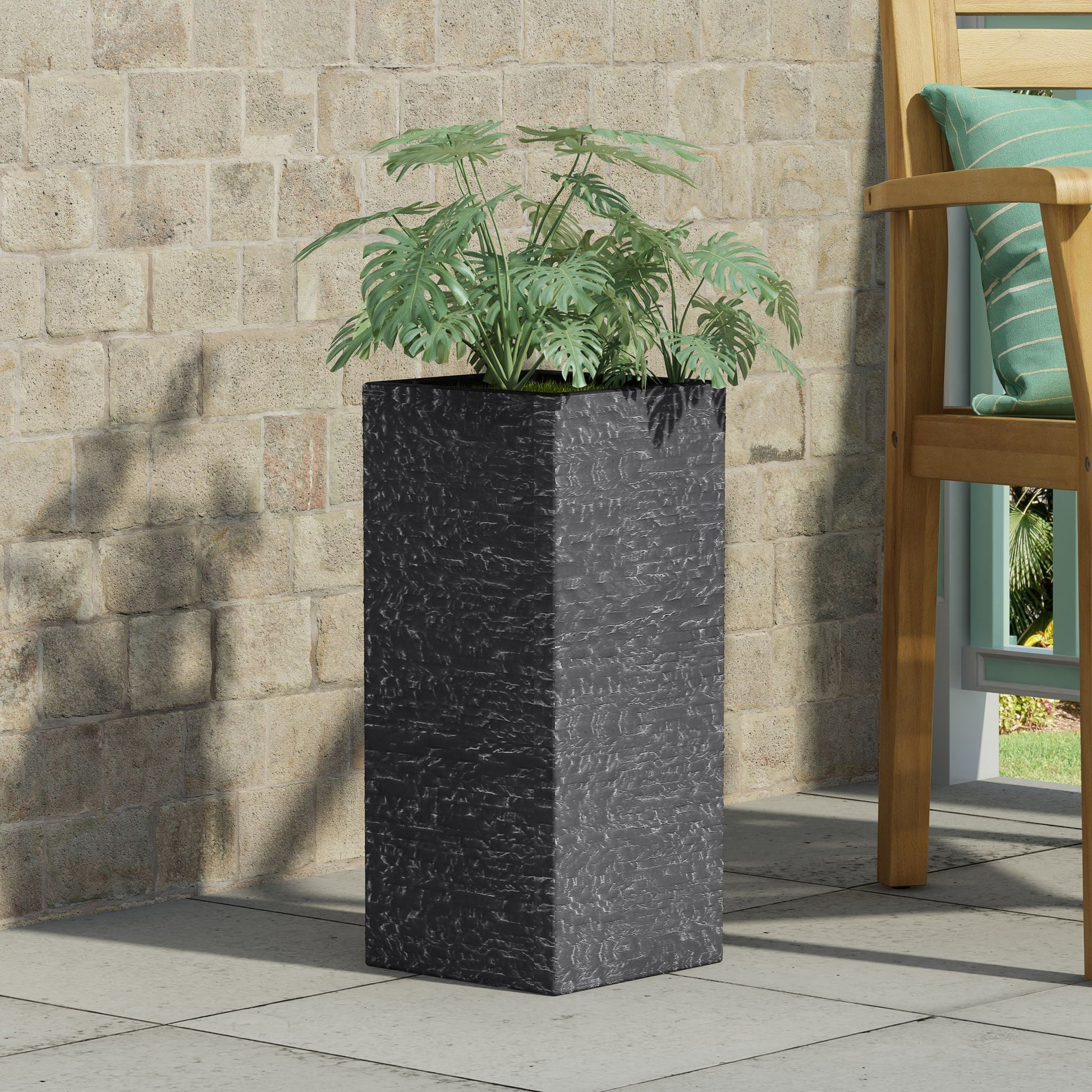 Black rectangular planter with green plants against a stone wall.