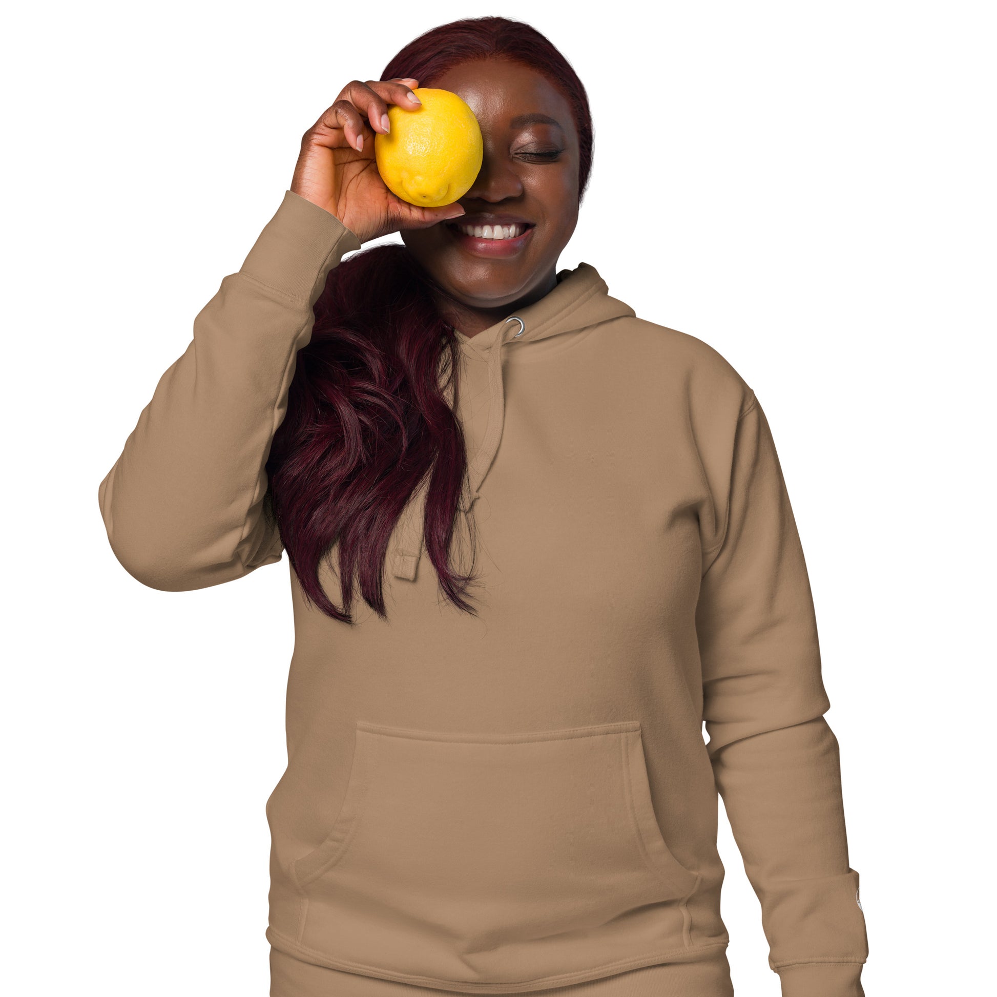 Person wearing a beige hoodie holding a yellow fruit against a white background