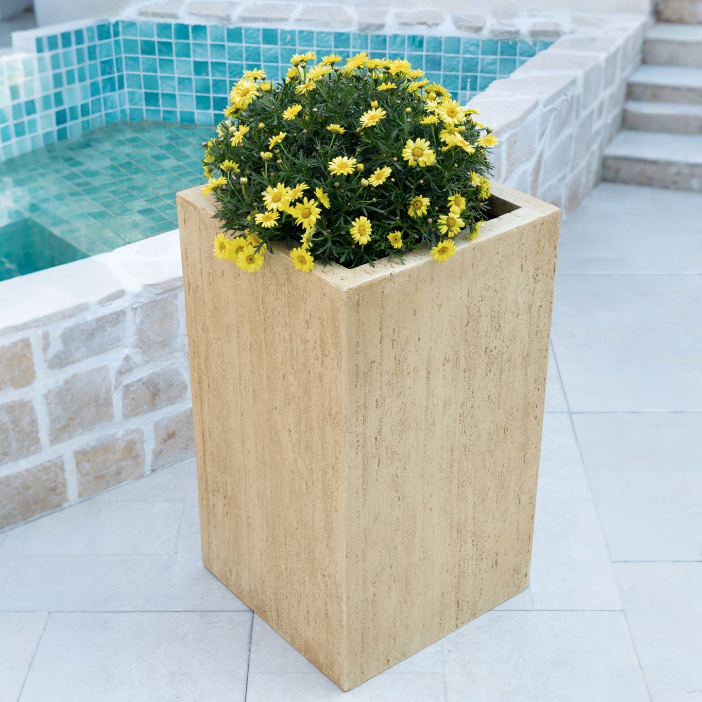Tall rectangular planter with yellow flowers by a poolside.