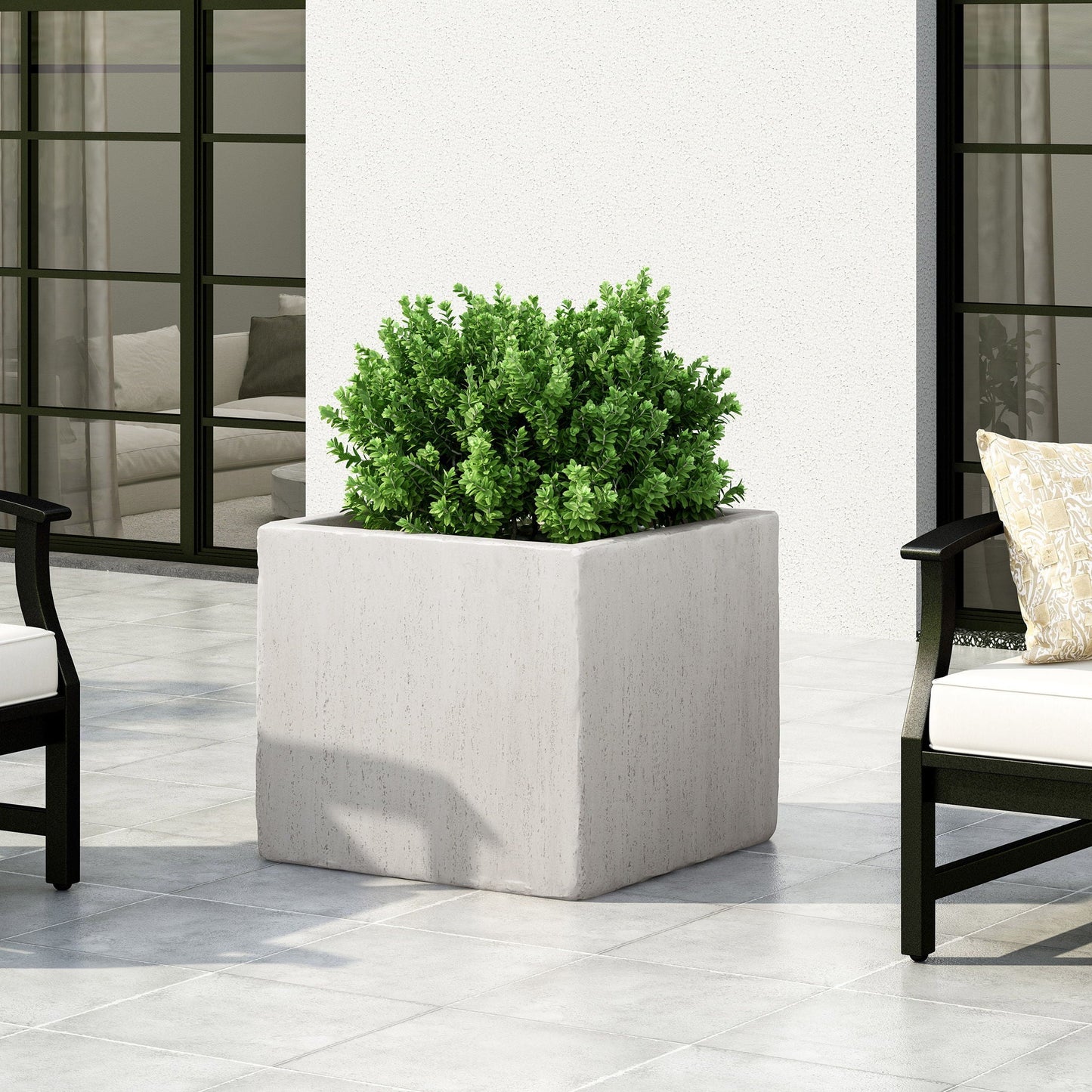 Square concrete planter with green plant on a patio with chairs and cushions.