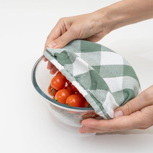 Green and white checkered cloth covering a bowl of tomatoes on a white background