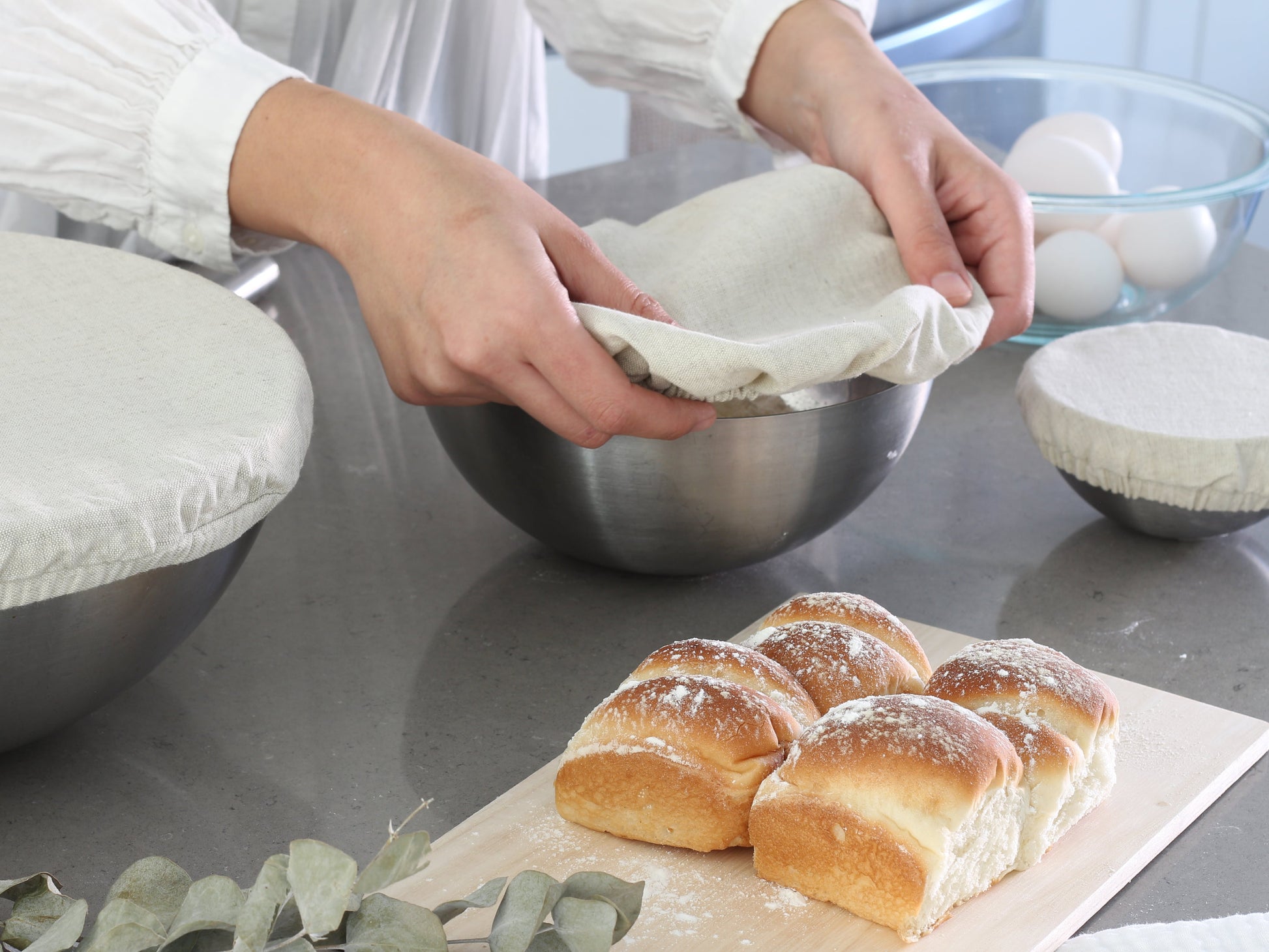 Baked bread rolls on a cutting board with a person preparing ingredients in the background.