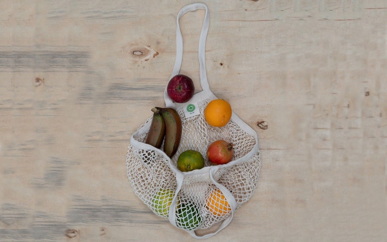 White mesh produce bag with fruits on a wooden surface